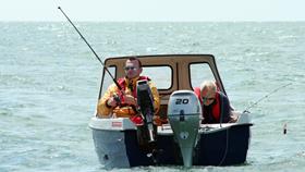 Two anglers fishing from a small boat and wearing lifejackets