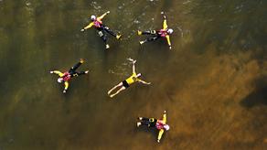 Four crew members and a GAA athlete float in the water, with their arms and legs spread.