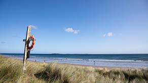 Life-ring on pole by beach with blue sky
