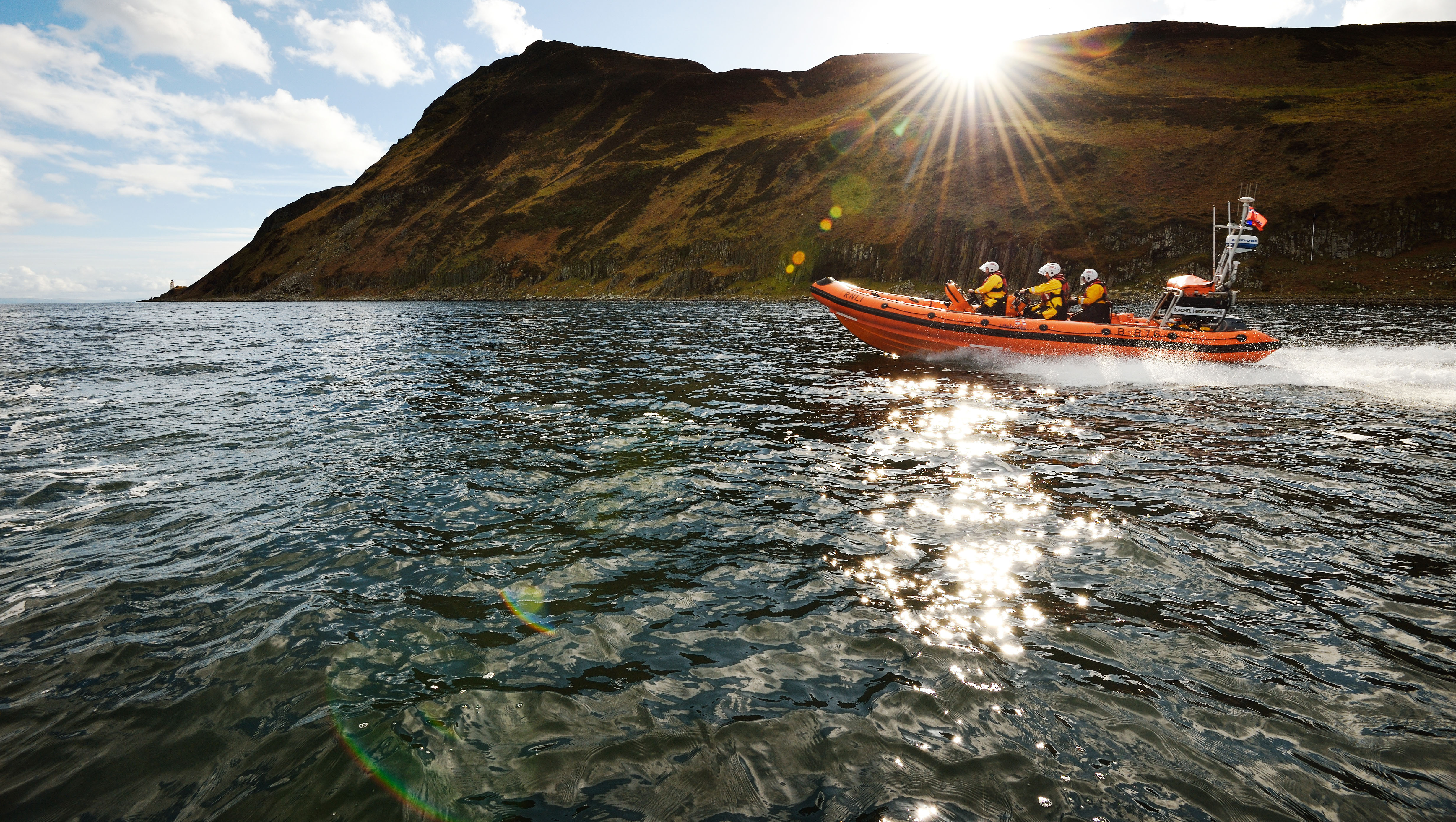 Arran RNLI’s Atlantic 85 inshore lifeboat at sea during a training exercise. It’s a blue day, with sun rays shining down on the lifeboat. 