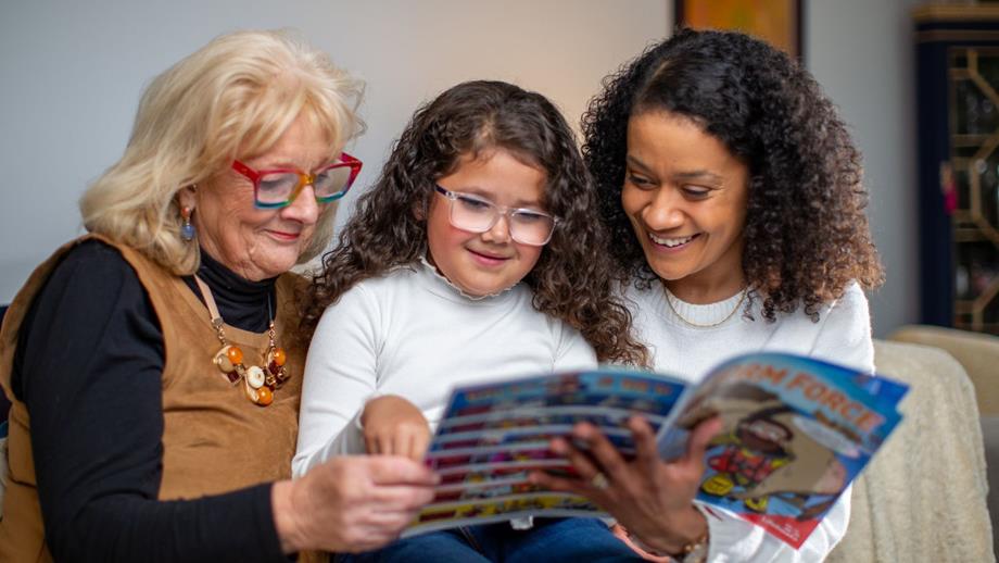 Two women and a child sat together on a sofa reading the Stormforce magazine. 