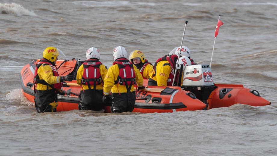 An RNLI crew, some standing waist-deep in water, prepare their D class inshore lifeboat