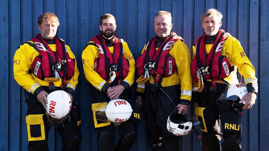Four Dart lifeboat volunteers stood outside of the boathouse all wearing full crew kit