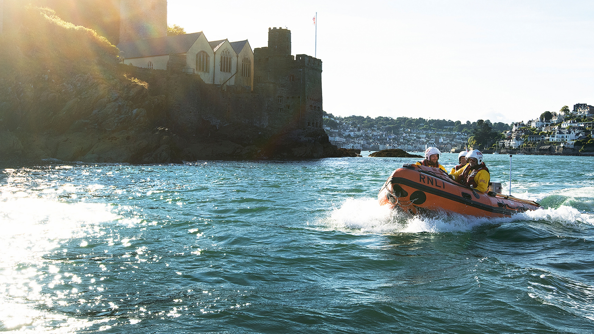 Dart lifeboat crew on the water at sunset in their D class Spirit of the Dart with Dartmouth on the horizon