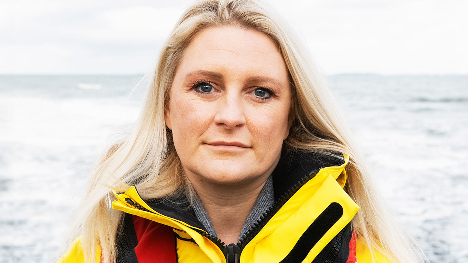 A portrait of Kate Morton, Volunteer Crew Member at Seahouses RNLI. She is wearing crew kit and the sea is in the background.
