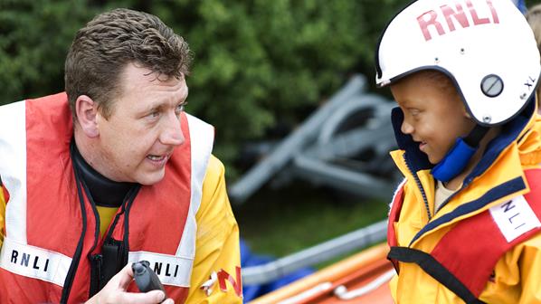 A volunteer crew member showing a child a handheld VHF radio at an RNLI education event in Legoland