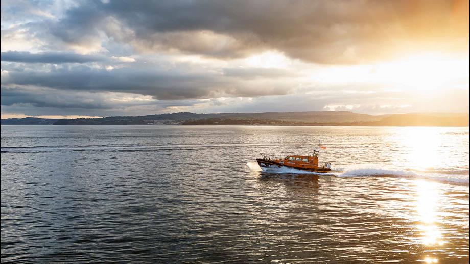 Exmouth's Shannon class lifeboat cruises along calm seas as the sun sets behind the coastline