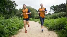 Two RNLI fundraisers running along a woodland track