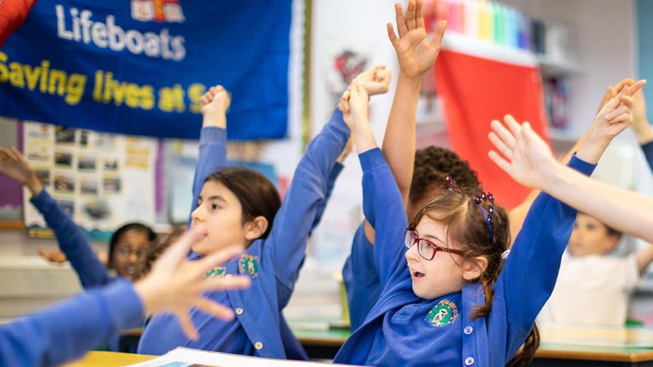 Children raising their arms in a school classroom during a visit by an RNLI education volunteer