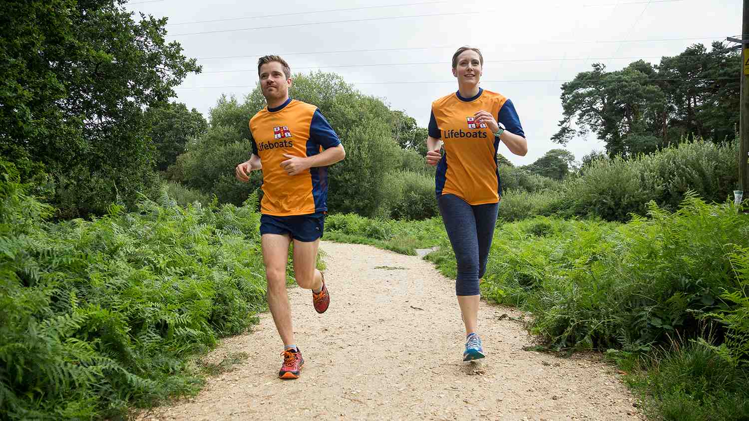 Two people running to raise money for the RNLI, in branded orange and navy-blue T-shirts