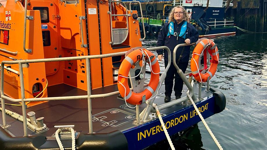Invergordon Launch Authority Jacqueline Macfarlane standing at the stern of the station’s Shannon class all-weather lifeboat. The lifeboat is moored and Jac is wearing a blue RNLI lifejacket.