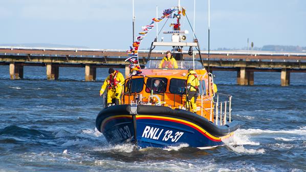 The Invergordon lifeboat displaying bunting and with crew on the deck moves through some small waves.