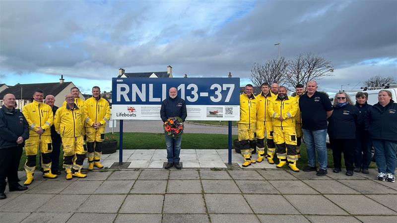 Invergordon volunteers paying their respects to all those named on their Shannon class lifeboat. They’re standing either side of the RNLI 13-37 lifeboat decal sign. Andrew Shepherd, Lifeboat Operations Manager, stands in front of the sign with a wreath.