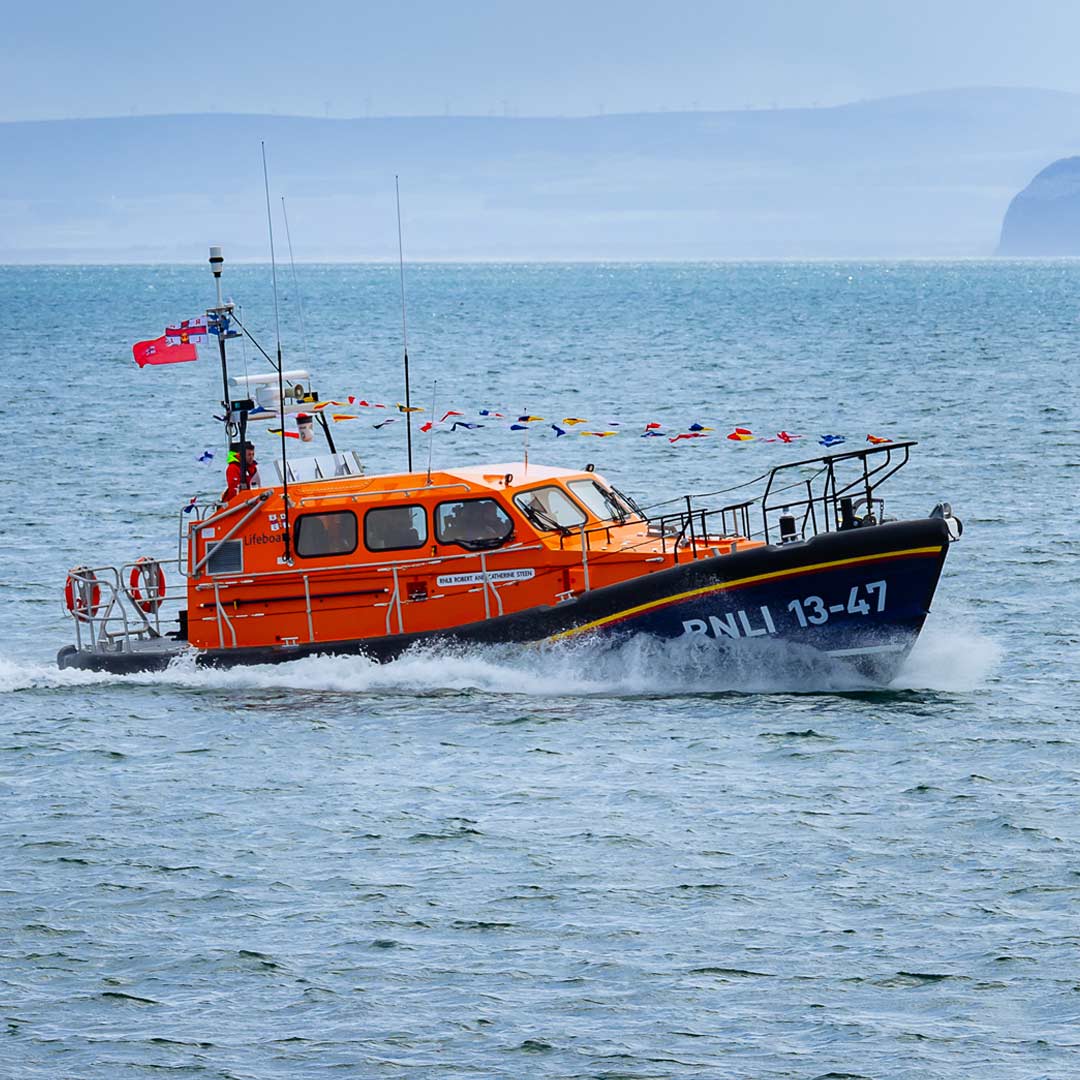 The Anstruther lifeboat creating a wake as it powers along with decorative bunting across the wheelhouse and deck.