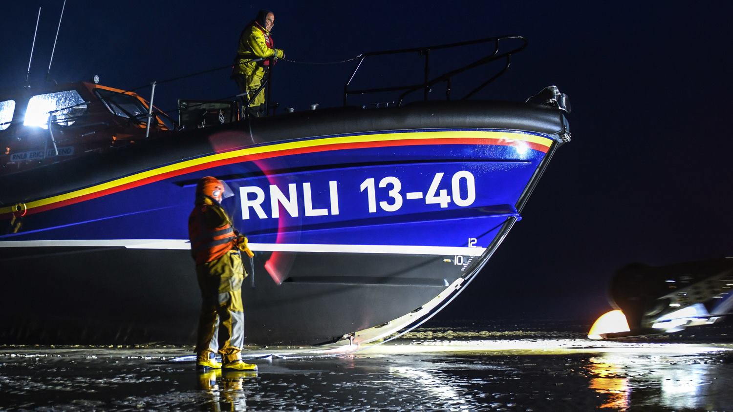 Eric's Legend lifeboat 13-40 in the dark, lit by floodlights, with crew members aboard