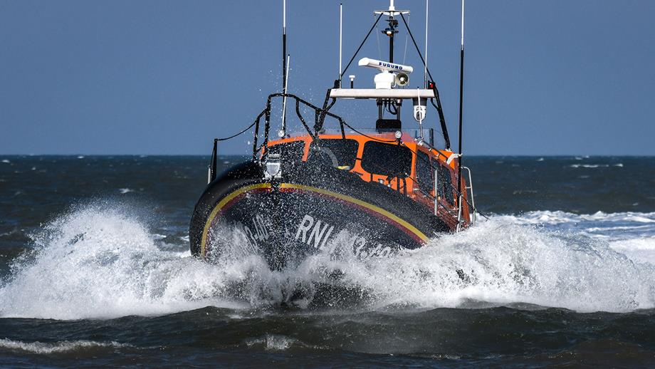 Shannon class all-weather lifeboat Eric’s Legend at sea, heading straight towards the camera. White surf surrounds the lifeboat as it powers through the sea. It’s a bright sunny day.