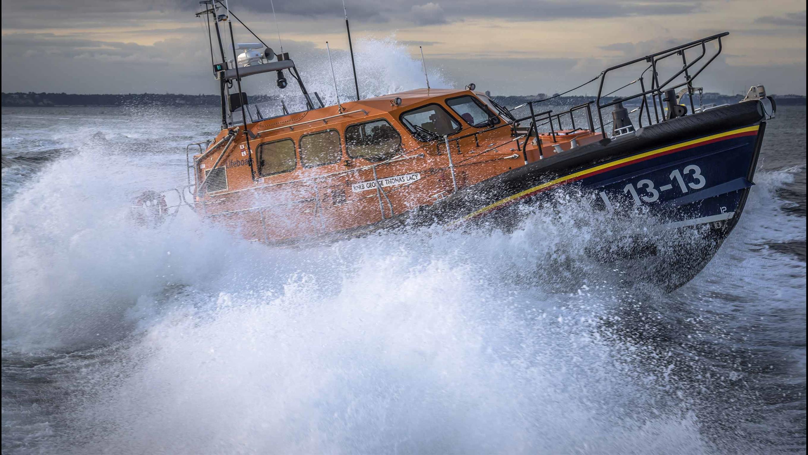 Swanage RNLI’s Shannon class lifeboat 13-13 powering through choppy water, surrounded by lots of white spray and dark clouds above 