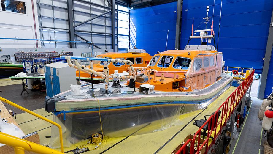A lifeboat under construction in a bright, industrial workshop with tools and materials around.