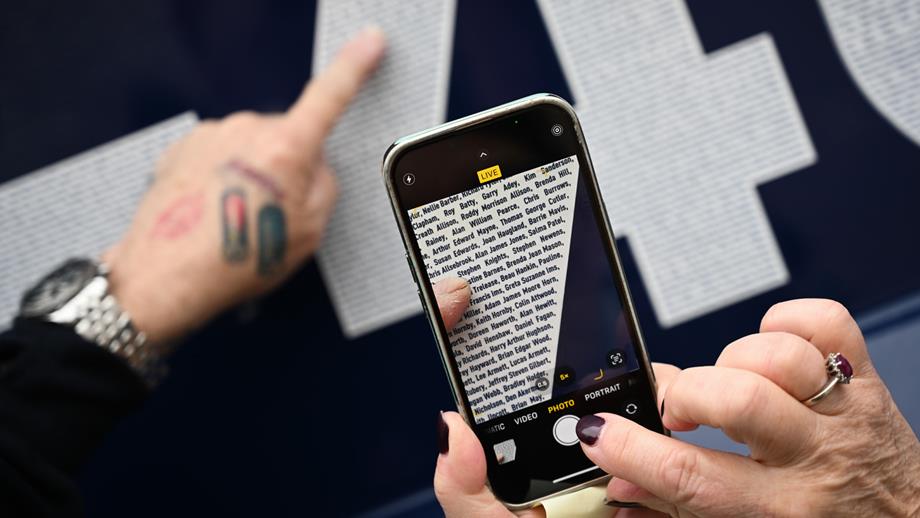 Launch a Memory event at the All-Weather Lifeboat Centre (ALC) in Poole. A hand points out a name, whilst another hand holds a phone and takes a photo. Members of the public viewing the  Shannon class lifeboat Eric's Legend 13-40, where the names of loved ones are printed on the lifeboat's decal.