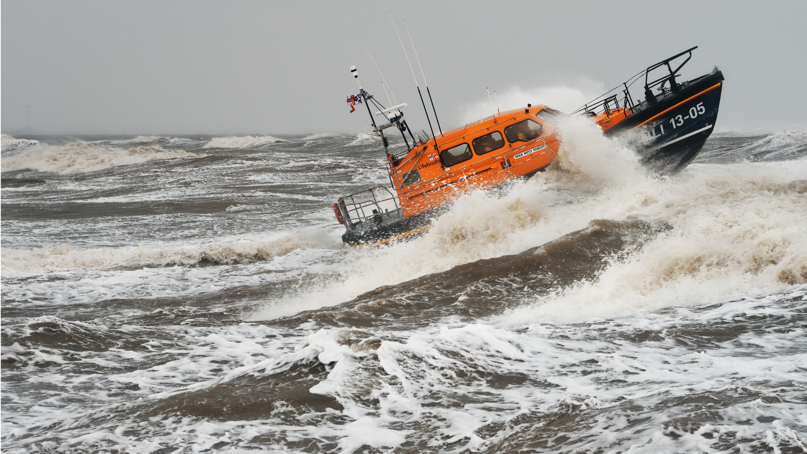 A Shannon class all-weather lifeboat moving through dark, rough seas, with waves crashing over the bow