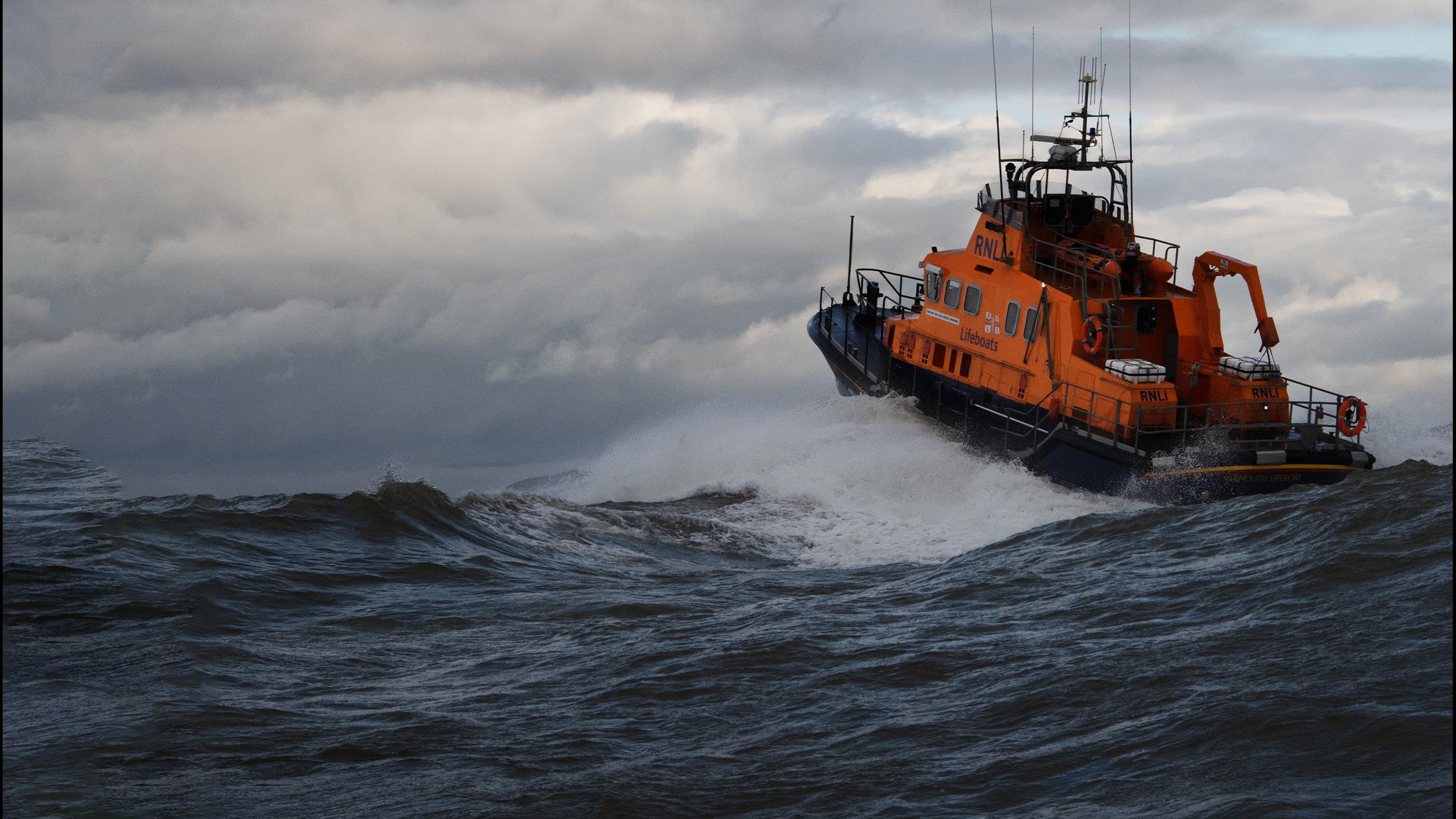 RNLI lifeboat moving through a wave towards a cloudy sky