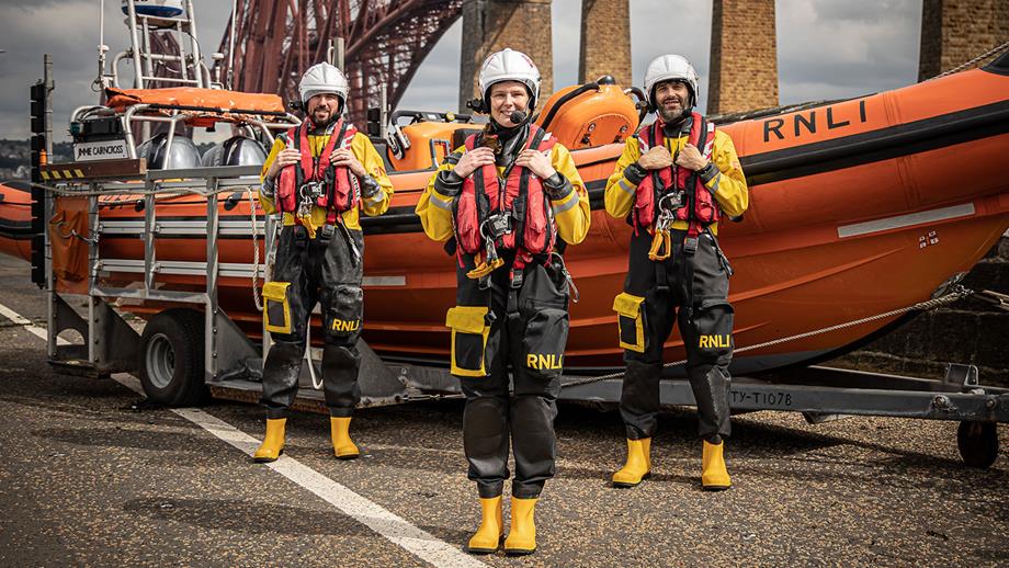 Three RNLI crew members in kit stand in front of a B Class Lifeboat