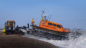 Relief Shannon class all-weather lifeboat Eric Legend 13-40 being launched on exercise at Dungeness Beach by the Shannon launch and recovery system (SLARS). Clear blue skies and spray from the surf as the lifeboat enters the water. Shingle beach.
