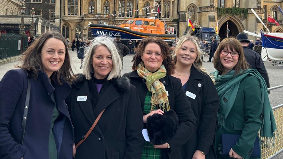Five female RNLI staff members are stood in front of a lifeboat and smiling.