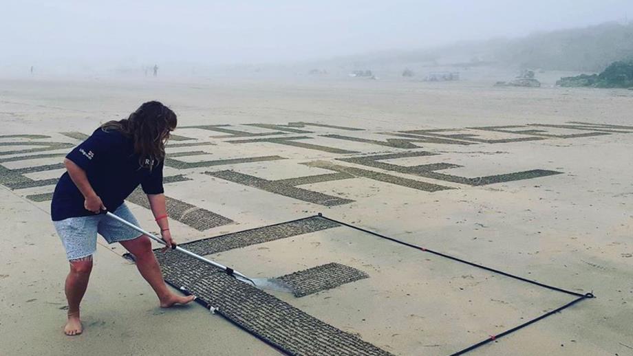 RNLI volunteer raking safety message into beach sand