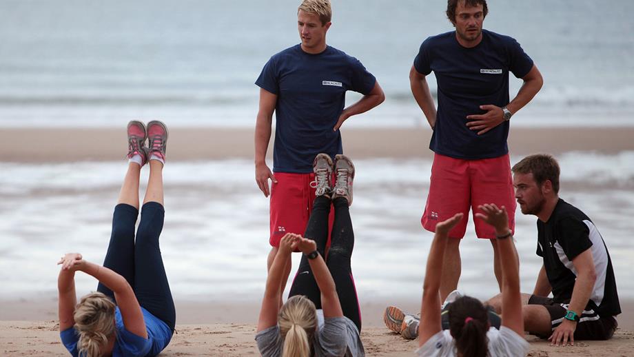 Three runners stretch on a sandy beach. Stretching and warming up before a run helps to prevent injury