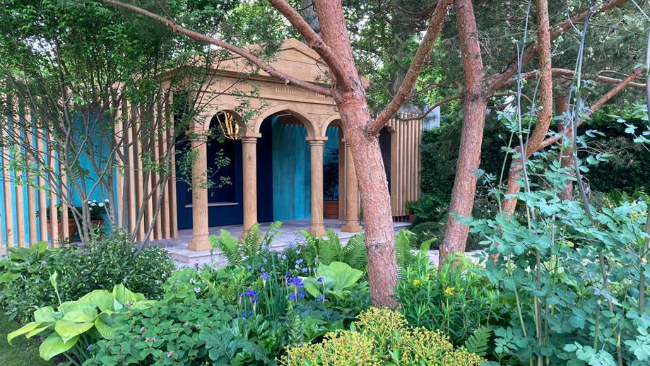 The RNLI’s garden at the RHS Chelsea Flower Show. There is a pavilion behind some green plants and trees.