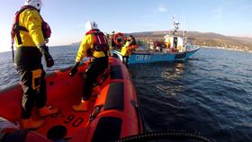 Helensburgh’s B class lifeboat approaches a blue fishing boat, where a fisherman is holding onto a man over the stern of the boat