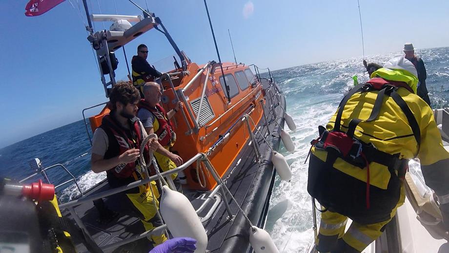 An RNLI crew member steps aboard the yacht to treat the injured man