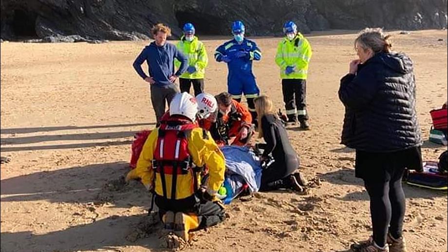 A woman lies on a stretcher, covered by a blanket, surrounded by RNLI crew and Coastguard Rescue Team volunteers