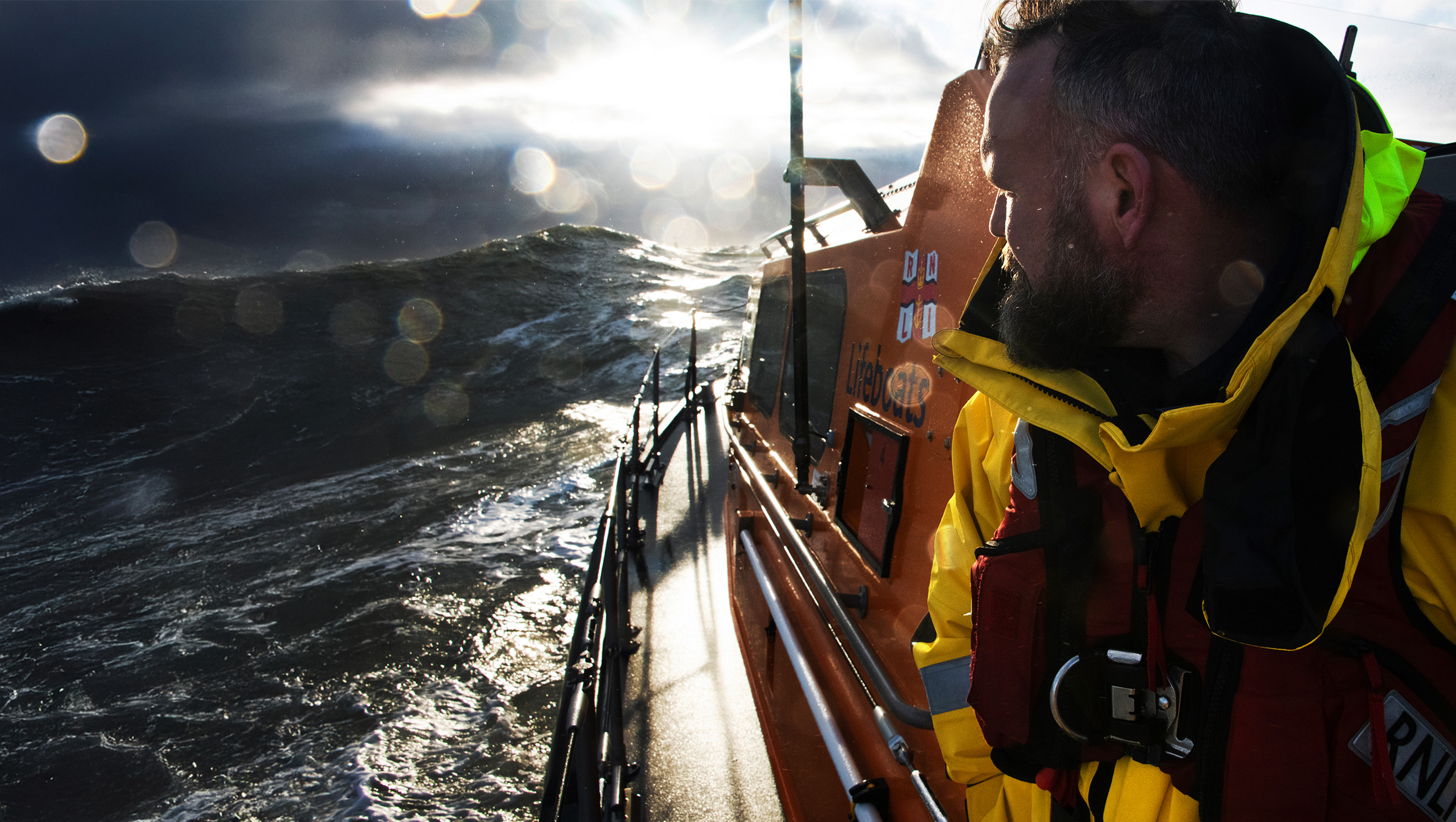 An RNLI crew member aboard a lifeboat looks back at the sea behind him