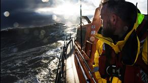 An RNLI crew member aboard a lifeboat looks back at the sea behind him