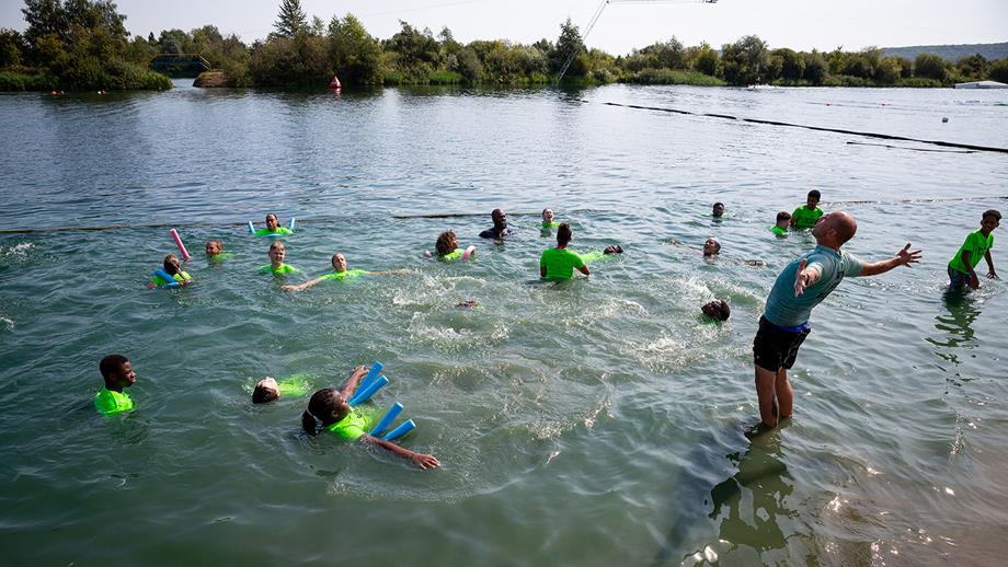 Children are in a lake and are being taught how to Float to Live by a Swim Safe instructor