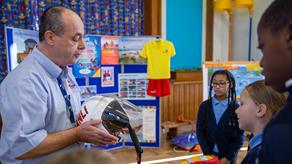 An RNLI water safety volunteer is holding a lifeboat crew helmet and teaching children about it