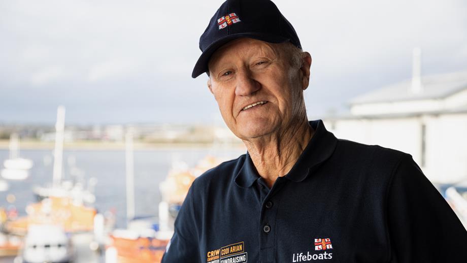 Fundraising Volunteer Chris Copeland with lifeboats in the background wearing his fundraising volunteer crew polo shirt