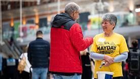 An RNLI fundraising volunteer, wearing a Mayday T-shirt, speaking to a member of the public while collecting donations.