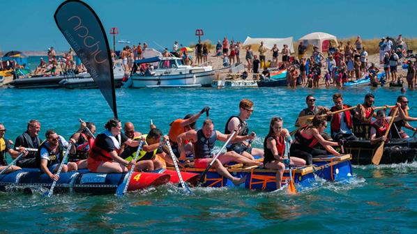 Three teams taking part in a raft race on the water.
