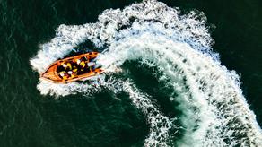 An inshore lifeboat is pictured from above. There are four crew members on board, and they are travelling in a curved direction, leaving a swirling trail of whitewash behind them.