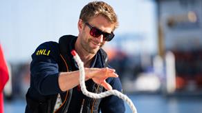 An RNLI trainer is wearing a lifejacket, sunglasses and an RNLI fleece and is catching a white rope.
