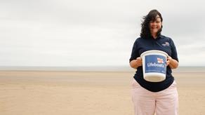 Barry Island Shop Volunteer Avril Kitchen stood on the beach holding a collection bucket.