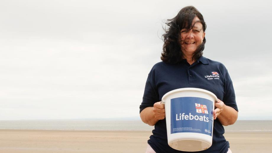 Barry Island Shop Volunteer Avril Kitchen stood on the beach holding a collection bucket.