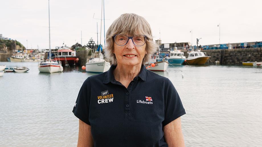 Newquay Shop Volunteer Carol Hudson smiling, with boats on the water in the background.