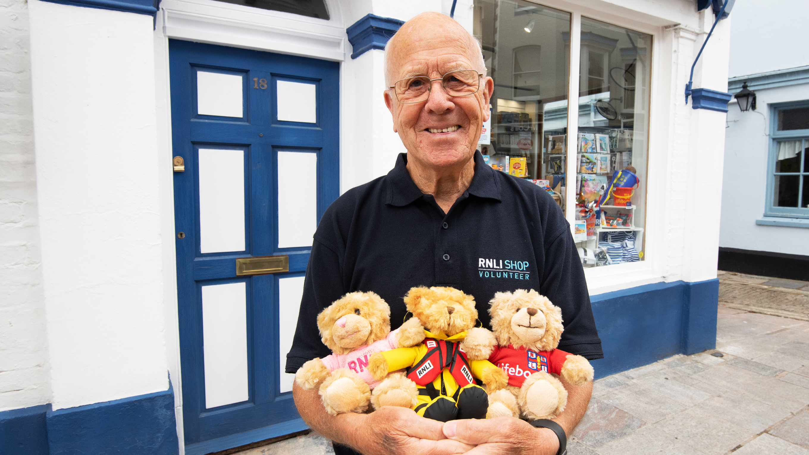 A retail volunteer standing outside an RNLI shop holding three teddy bears.