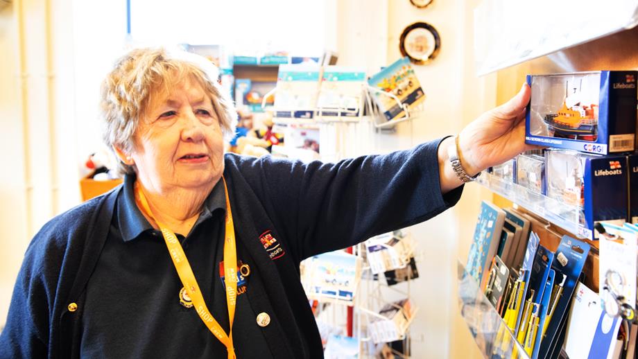 An RNLI shop volunteer stood next to a product display stand.