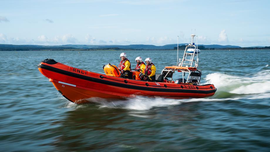 Three crew members onboard a D class inshore lifeboat on a clear day.