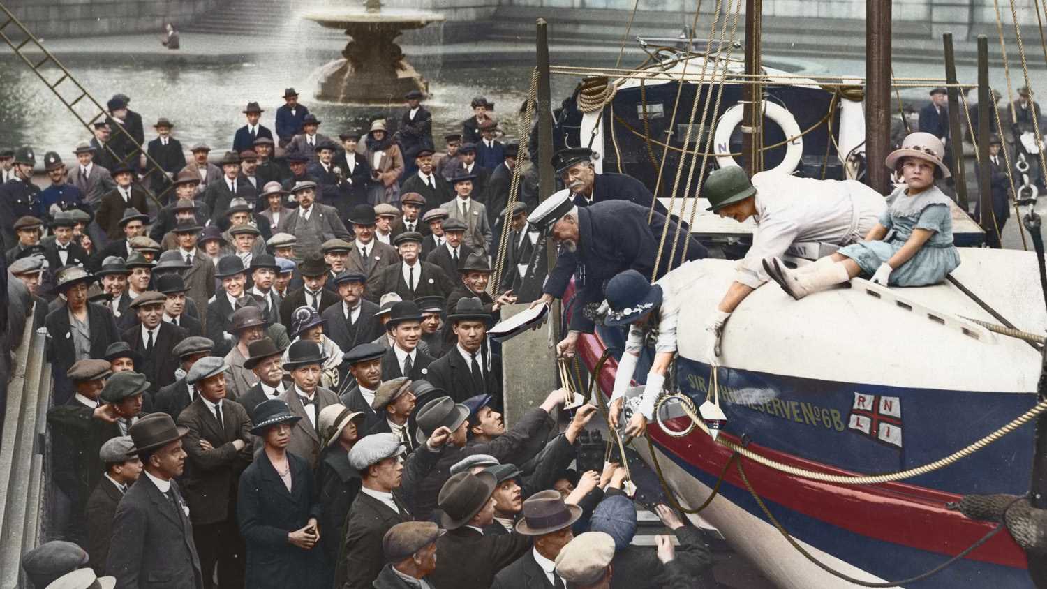 Celebrating the 100th anniversary of the RNLI, with a lifeboat in Trafalgar Square, London,  surrounded by members of the public wearing hats